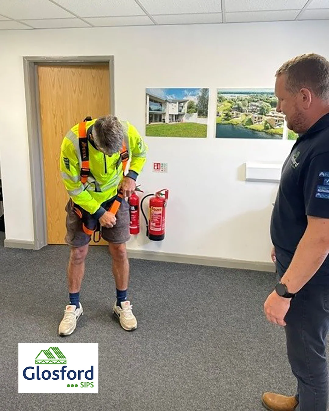 Worker in high-visibility jacket adjusts safety harness as colleague watches, fire extinguishers on wall and Glosford SIPS logo.