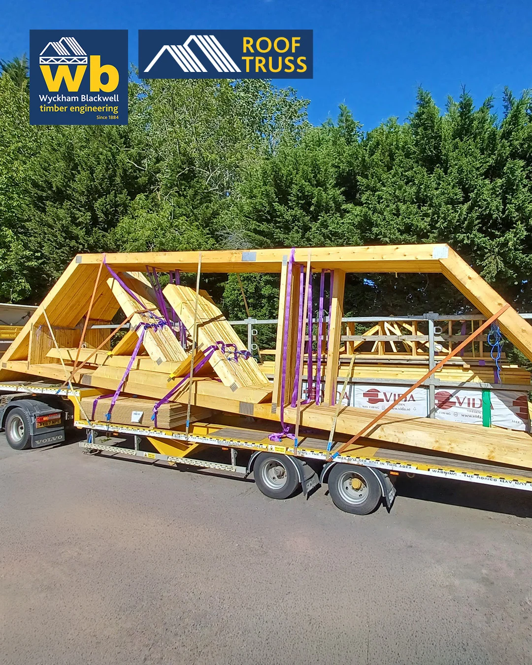 Yellow Wyckham Blackwell flatbed lorry with timber roof truss strapped on the back