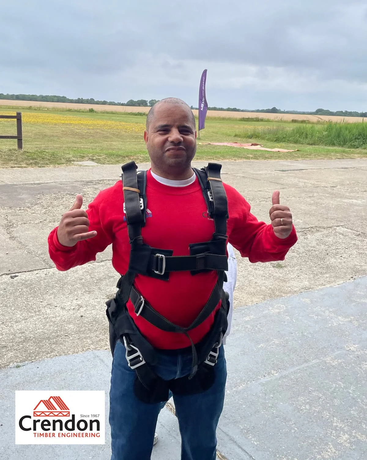 Man in a red Crendon jumper with his thumbs up, with skyddiving gear on